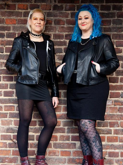 Diana Ringelsiep und Ronja Schwikowski stehen in punk-typischer Aufmachung vor einer Backsteinmauer und schauen in die Kamera.