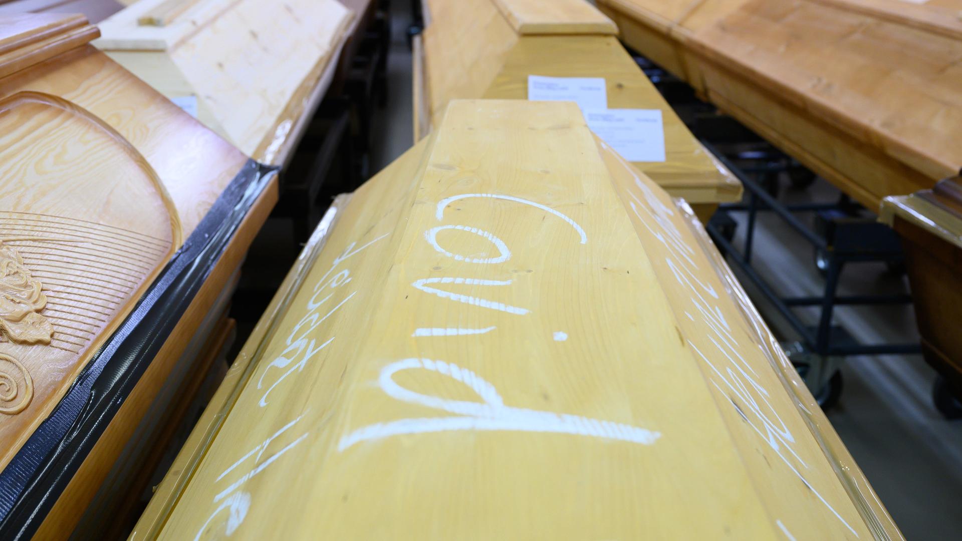 Ein Holzsarg mit Kreideaufschrift "Covid", daneben und im Hintergrund weitere Särge