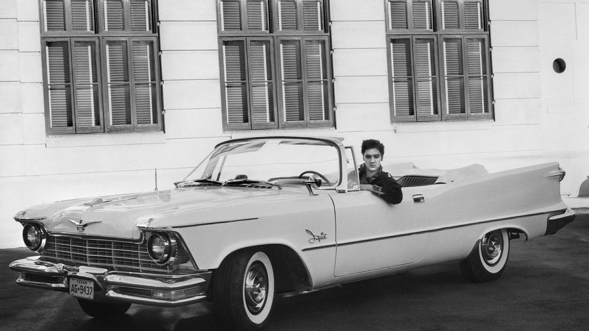 Der Sänger Elvis Presley in seinem Chrysler Imperial auf dem Studiogelände der Filmproduktionsfirma MGM in Hollywood, USA (1958). Sein Auto ist ein großes, weißes Cabriolet, das Verdeck ist geöffnet. Der Sänger Elvis Presley in seinem Chrysler Imperial auf dem Studiogelände der Filmproduktionsfirma MGM in Hollywood, USA (1958). Sein Auto ist ein großes, weißes Cabriolet, das Verdeck ist geöffnet.