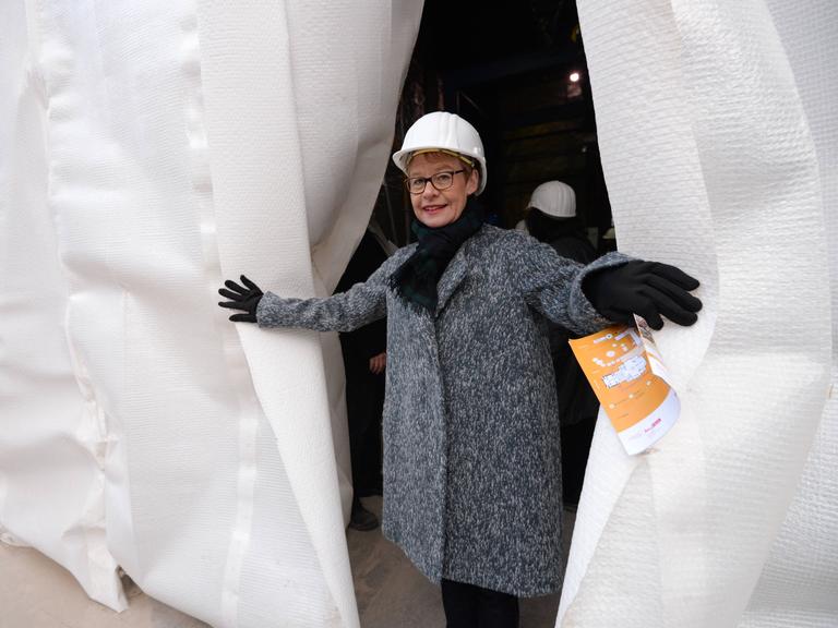Die ehemalige Senatsbaudirektorin Regula Lüscher mit Bauarbeiterhelm schaut hinter einem Vorhang hervor anläßlich des Beginns der Sanierung der Staatsoper Unter den Linden im Dezember 2014.