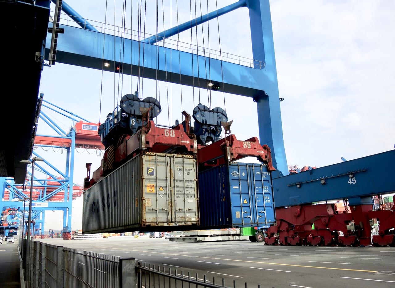 Zwei Container hängen an den Greifern einer Containerbrücke und werden auf das Kai abgelassen Zwei Container hängen an den Greifern einer Containerbrücke und werden auf das Kai abgelassen