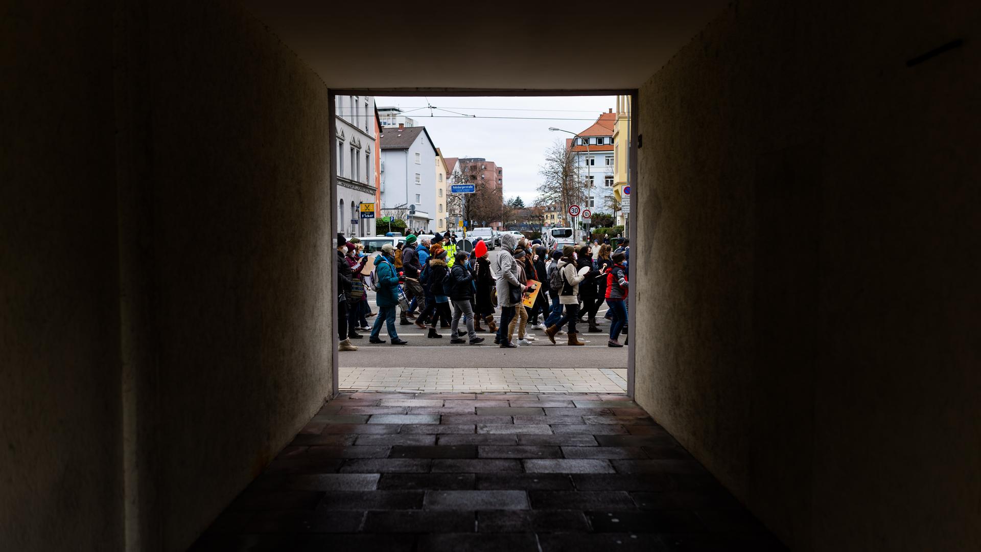 Blick durch eine dunkle Hauseinfahrt auf die Teilnehmerinnen und Teilnehmer einer Demonstration. Blick durch eine dunkle Hauseinfahrt auf die Teilnehmerinnen und Teilnehmer einer Demonstration.