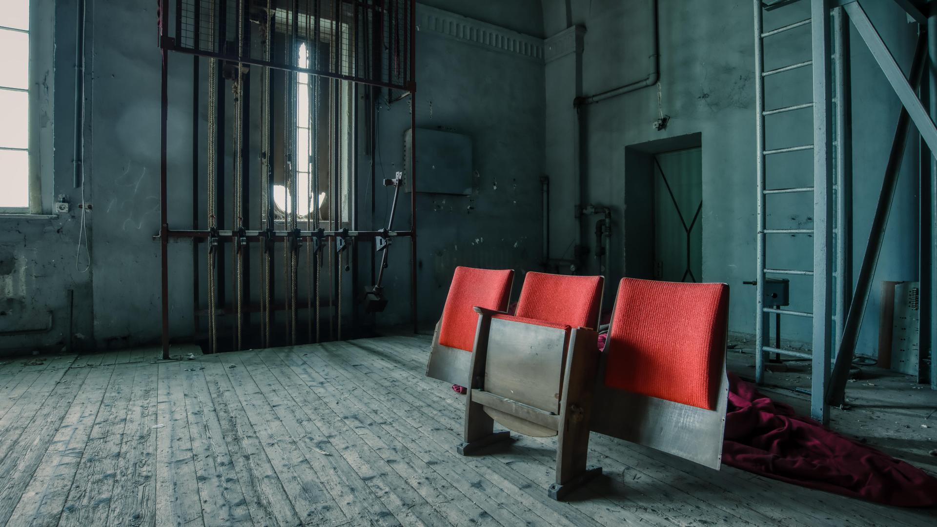 Drei Zuschauerstühle stehen hinter der Bühne eines verlassenen Theaters. Drei Zuschauerstühle stehen hinter der Bühne eines verlassenen Theaters.