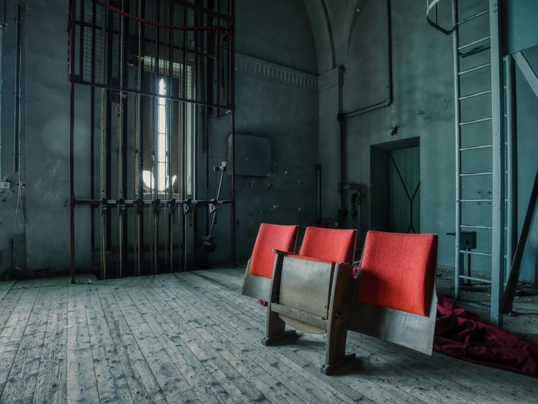 Drei Zuschauerstühle stehen hinter der Bühne eines verlassenen Theaters.