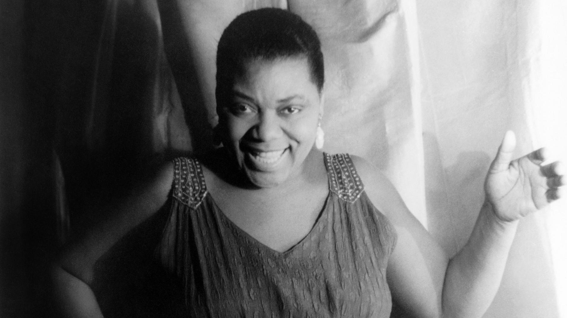Die afroamerikanische Bluessängerin Bessie Smith in einem schwarzweißen Porträtm am 3. Februar 1936. Die Sängerin trägt ein langes Kleid, kurze Haare und lächelt. Die afroamerikanische Bluessängerin Bessie Smith in einem schwarzweißen Porträtm am 3. Februar 1936. Die Sängerin trägt ein langes Kleid, kurze Haare und lächelt.