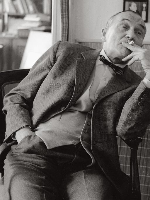 Heimito von Doderer zurückgelehnt auf einem Stuhl sitzend und Zigarette rauchend in seinem Wohnhaus in Wien.