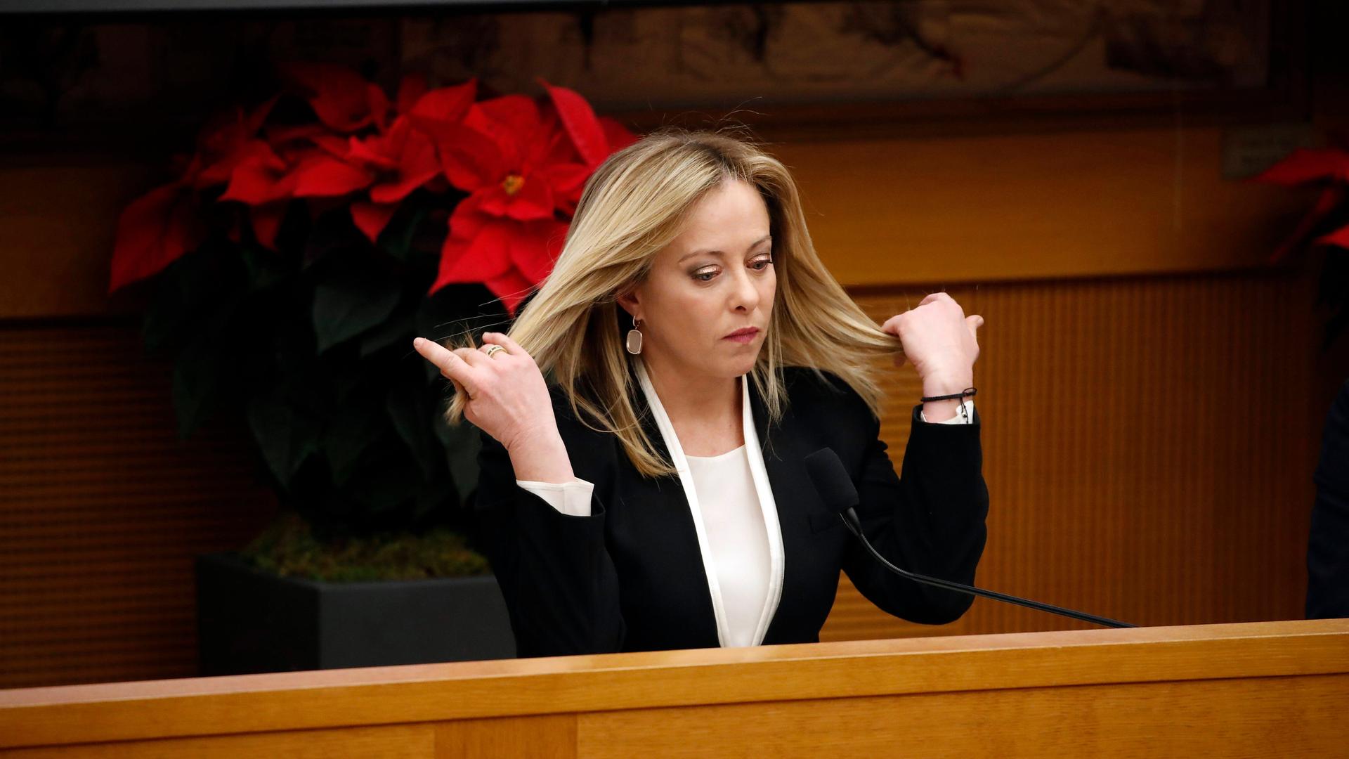Giorgia Meloni steht an einem Pult im italienischen Parlament und fährt sich mit den Händen durch die langen blonden Haare. Giorgia Meloni steht an einem Pult im italienischen Parlament und fährt sich mit den Händen durch die langen blonden Haare.