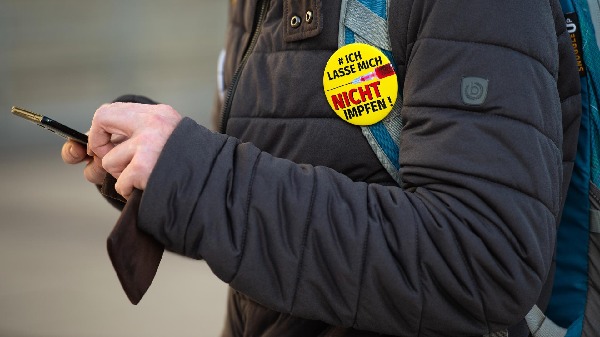 "Querdenker" Anti-Lockdown Protest in Leipzig. Ein Demonstrant trägt den Button: "#ich lasse mich nicht impfen" am Rucksack und tippt in sein Smartphone, 06.11.2021. "Querdenker" Anti-Lockdown Protest in Leipzig. Ein Demonstrant trägt den Button: "#ich lasse mich nicht impfen" am Rucksack und tippt in sein Smartphone, 06.11.2021.