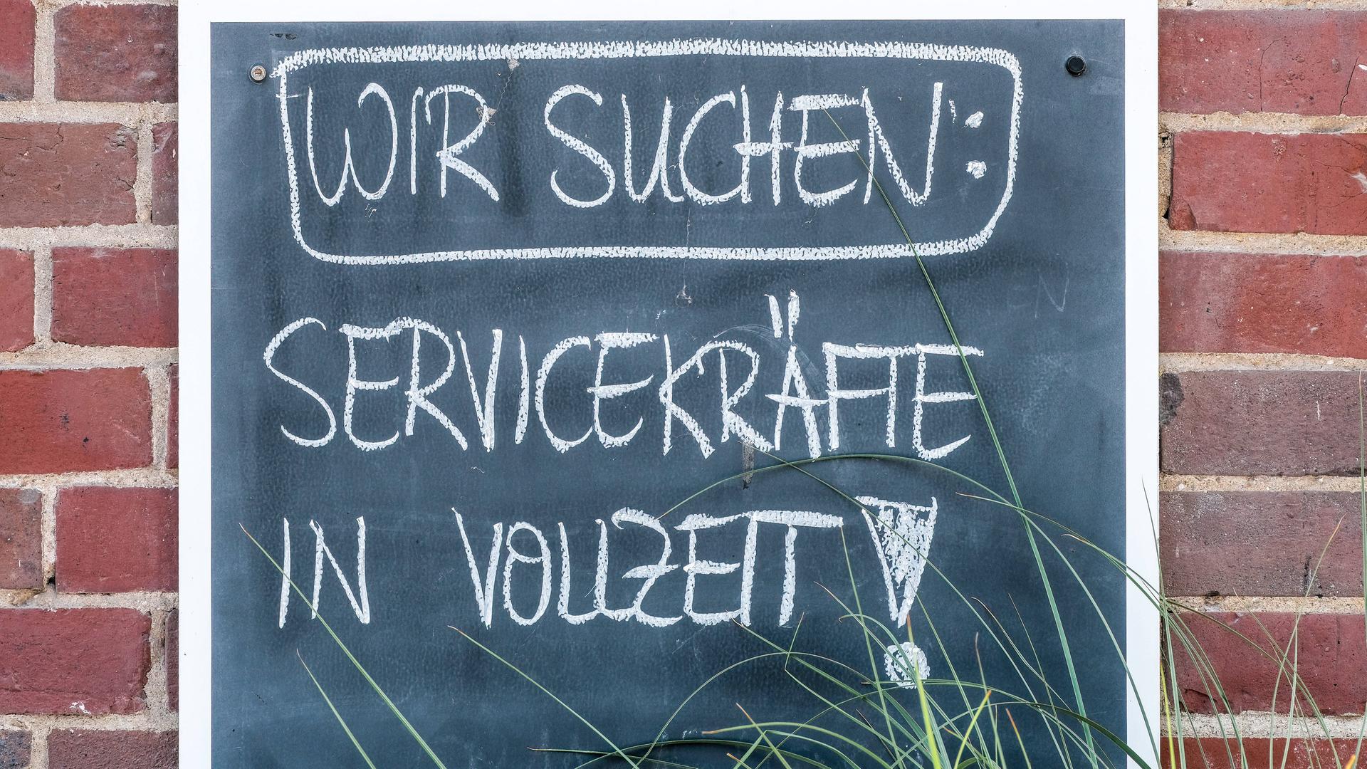 Auf einem Schild steht mit Kreide geschrieben: Wir suchen Servicekräfte in Vollzeit Auf einem Schild steht mit Kreide geschrieben: Wir suchen Servicekräfte in Vollzeit