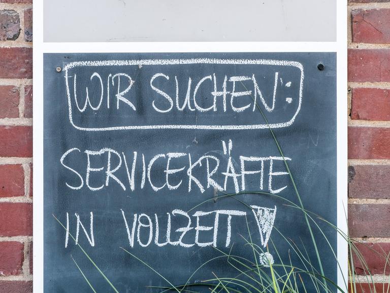 Auf einem Schild steht mit Kreide geschrieben: Wir suchen Servicekräfte in Vollzeit