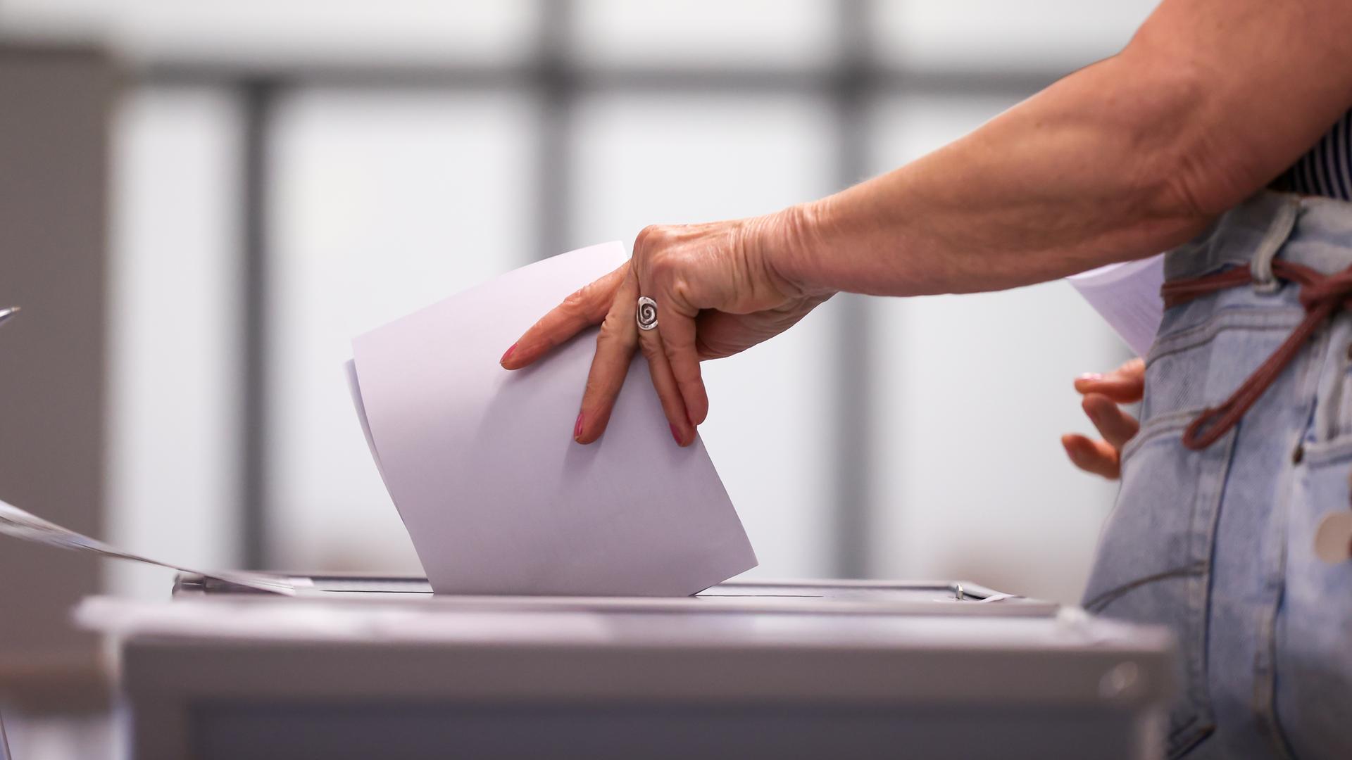 Eine Frau steckt einen Wahlschein in eine Urne. Eine Frau steckt einen Wahlschein in eine Urne.