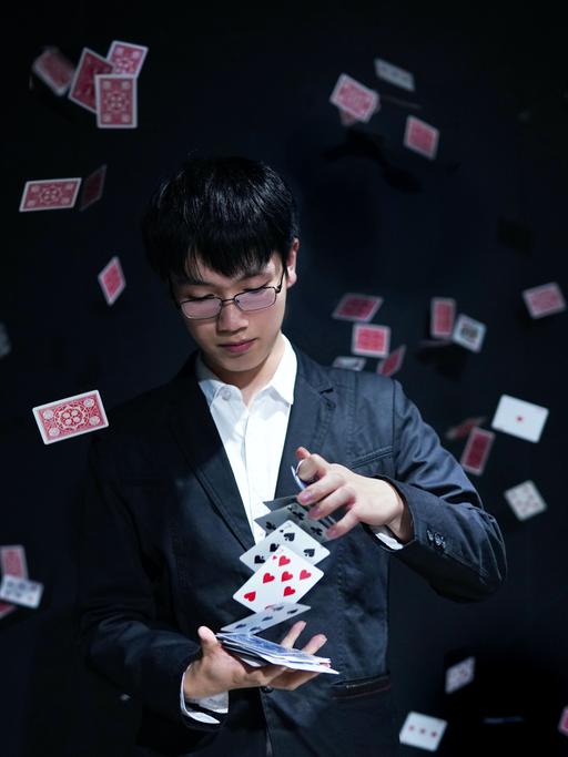 Ein junger Zauberer hält ein Kartenspiel in der Hand, um ihn herum fliegen einzelne Karten.