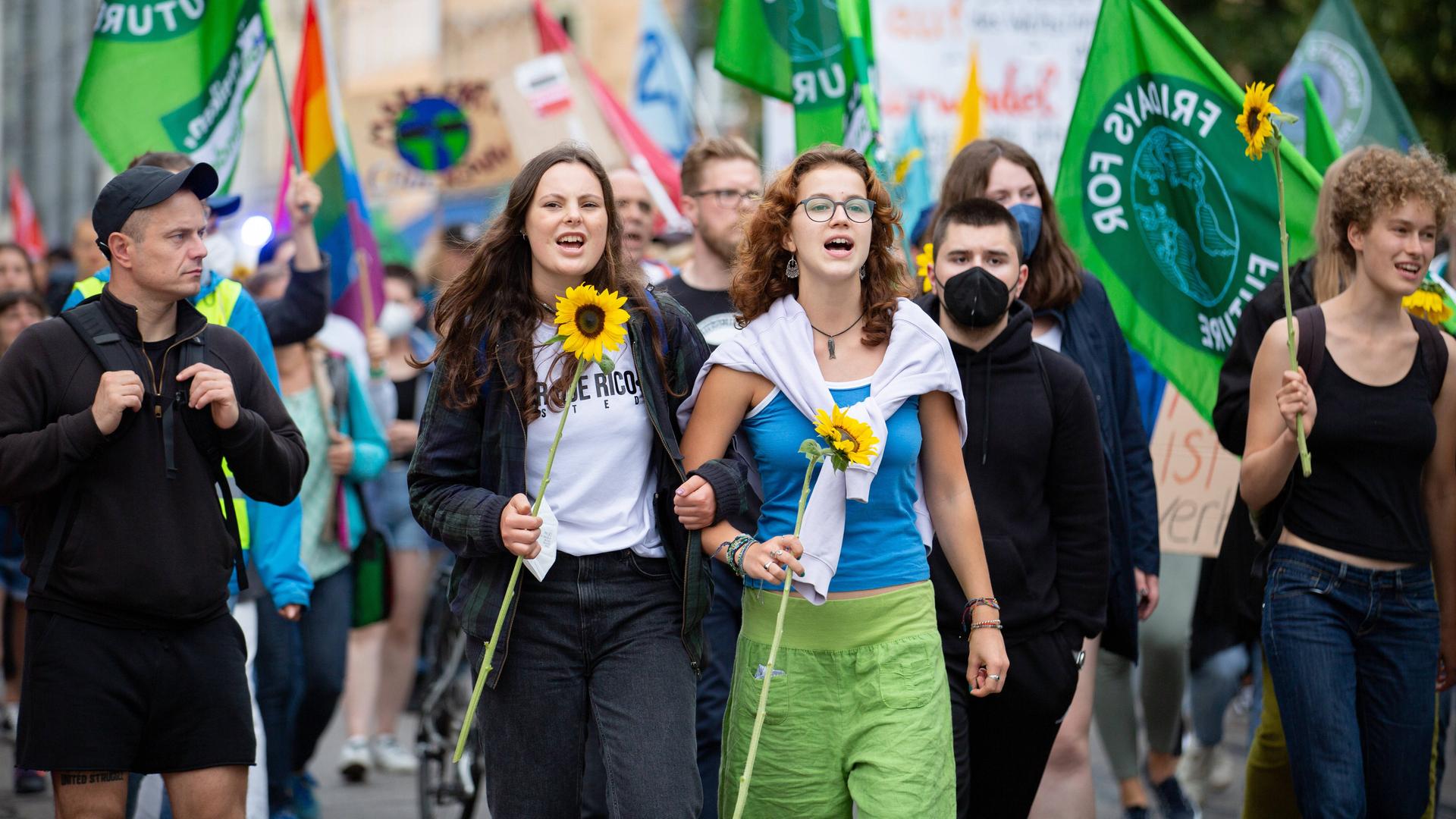 Zwei junge Frauen mit Sonnenblumen auf einer Demo. Im Hintergrund viele Fridays for Future-Fahnen. Zwei junge Frauen mit Sonnenblumen auf einer Demo. Im Hintergrund viele Fridays for Future-Fahnen.