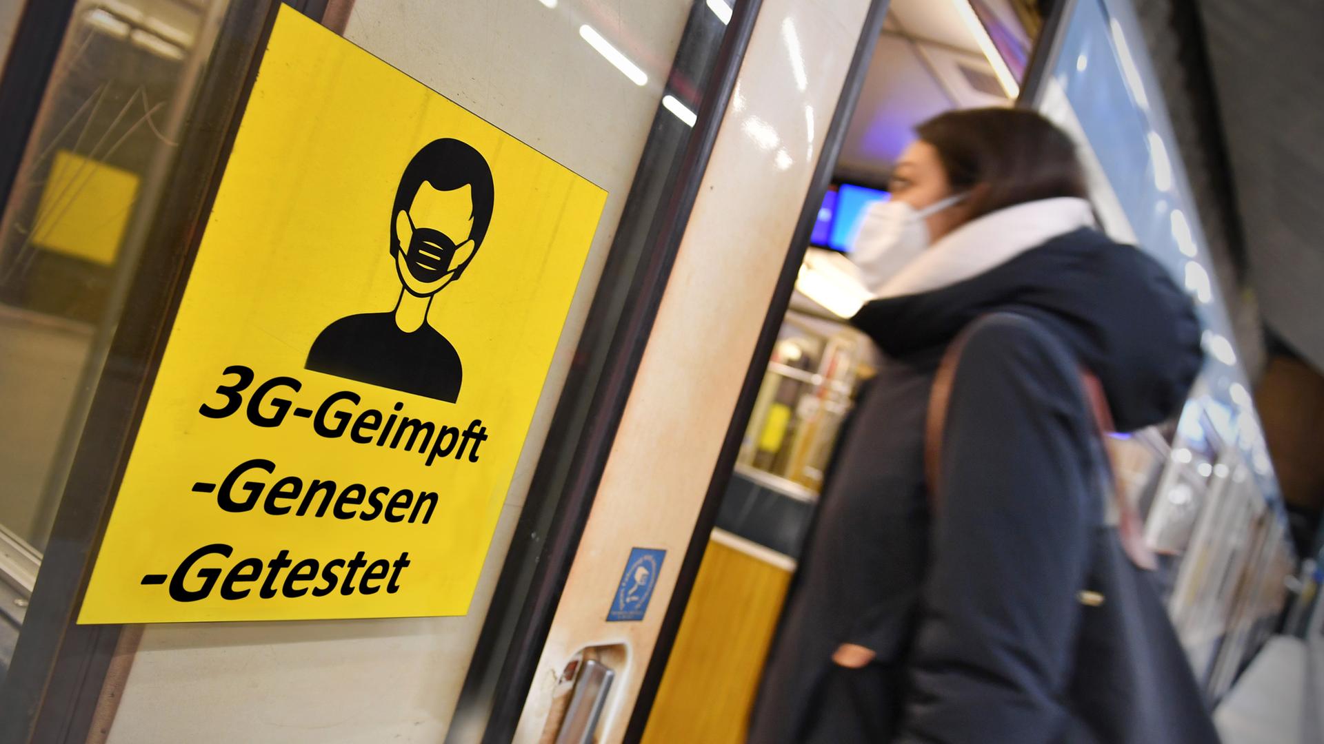 Eine Frau mit Maske steigt in einen Zug. An der Tür hängt ein Hinweis-Schild für die 3G-Regel.