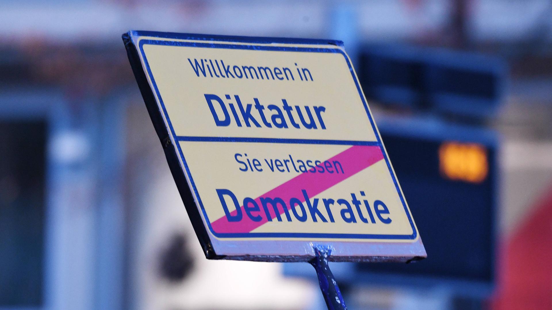Auf einem Schild bei einer Demonstration der Querdenken-Bewegung steht "Willkommen in der Diktatur - Sie verlassen Demokratie".