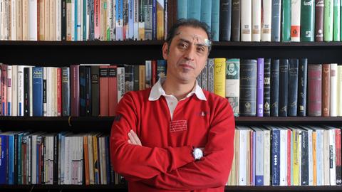 Madjid Mohit vom Sujet Verlag steht vor einem Regal mit einigen der von ihm verlegten Bücher.